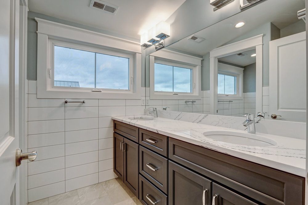 Bathroom with white tile, dark brown vanity, and two sinks under a large mirror and windows.