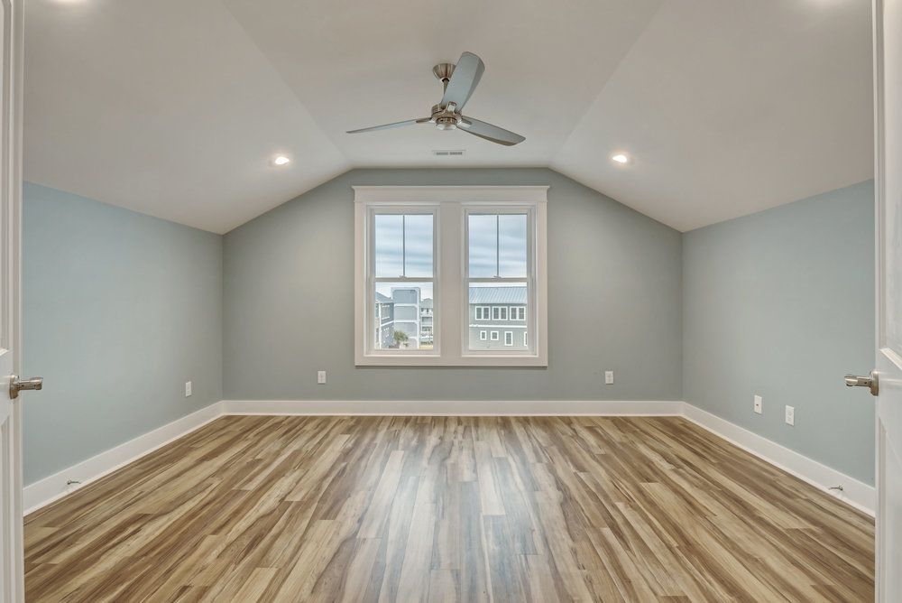 Empty room with light blue walls, wood-look floor, window, and ceiling fan.