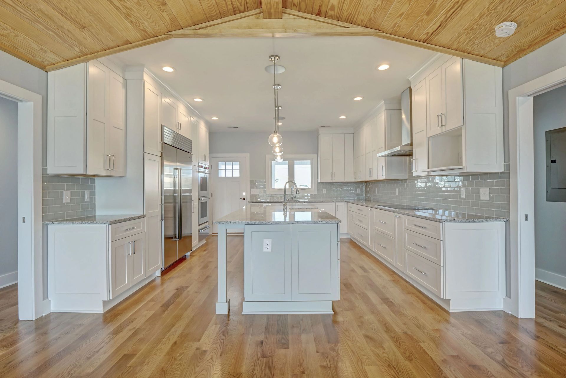 Modern white kitchen with island, wood floor, and wooden ceiling detail.
