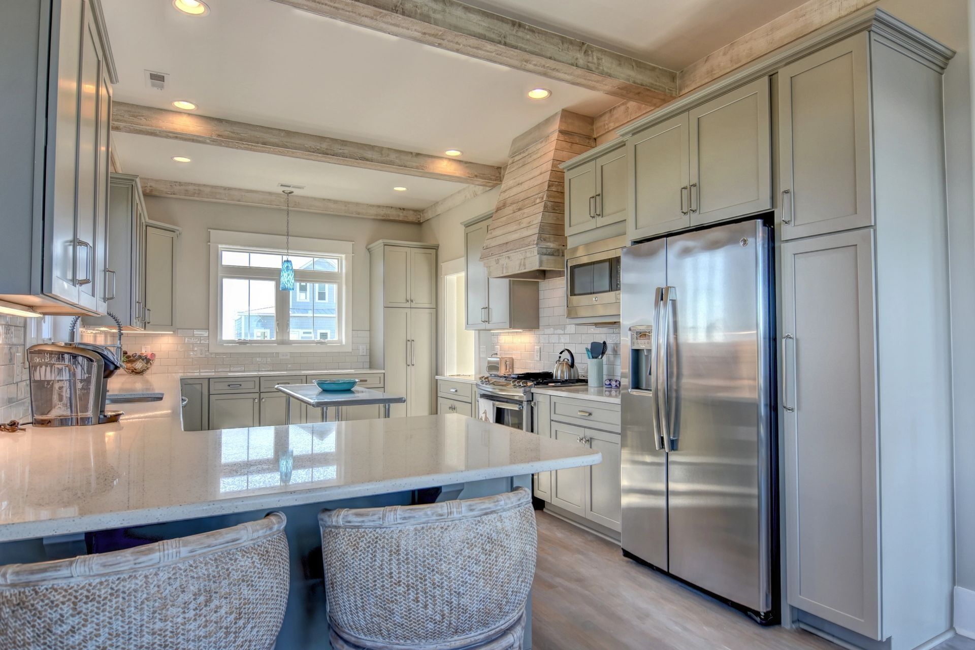 Light gray kitchen with stainless steel appliances, white countertops, and wood beams.