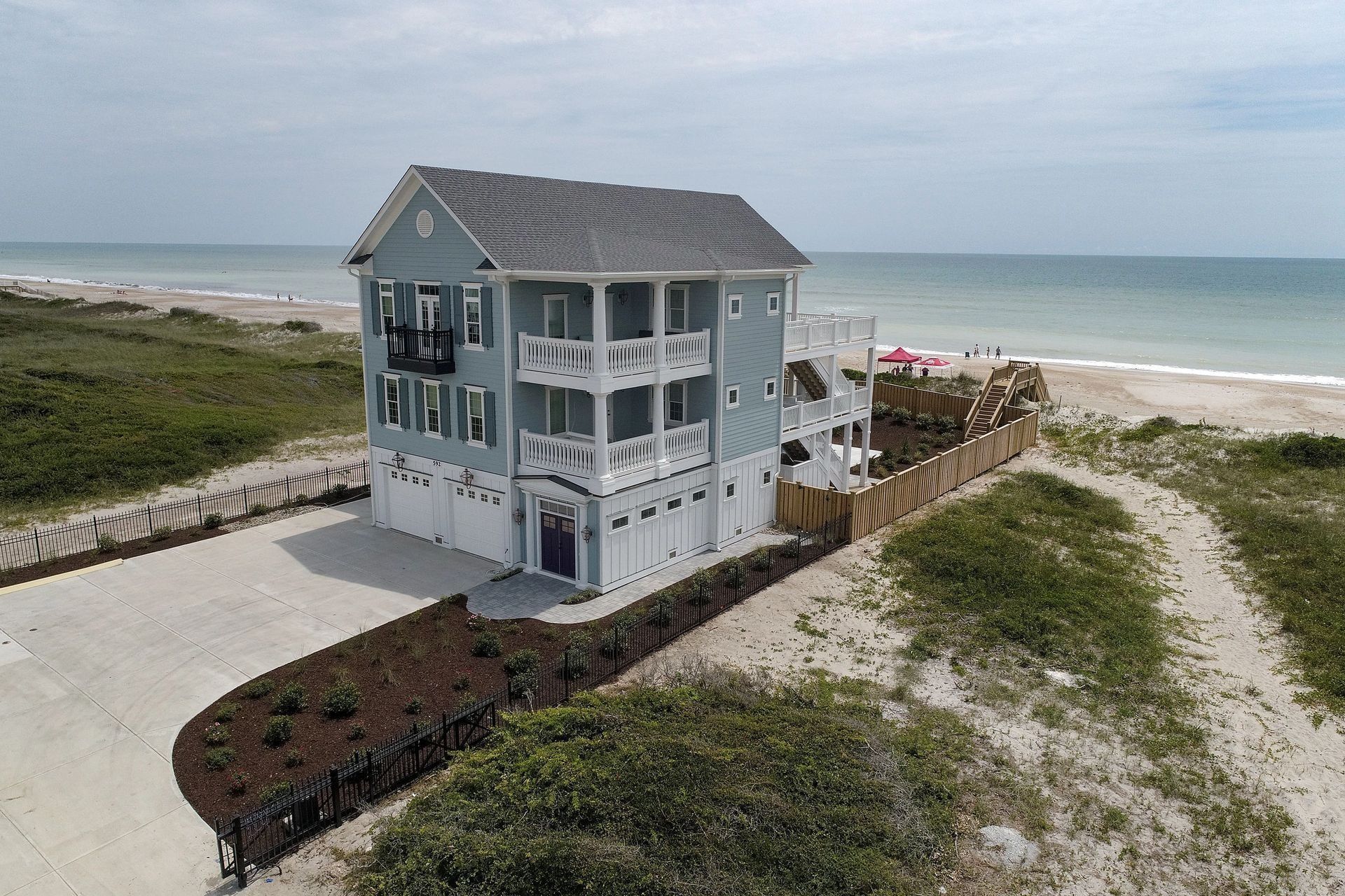 Beach house with light blue siding, multiple balconies, and a driveway leading to the ocean.