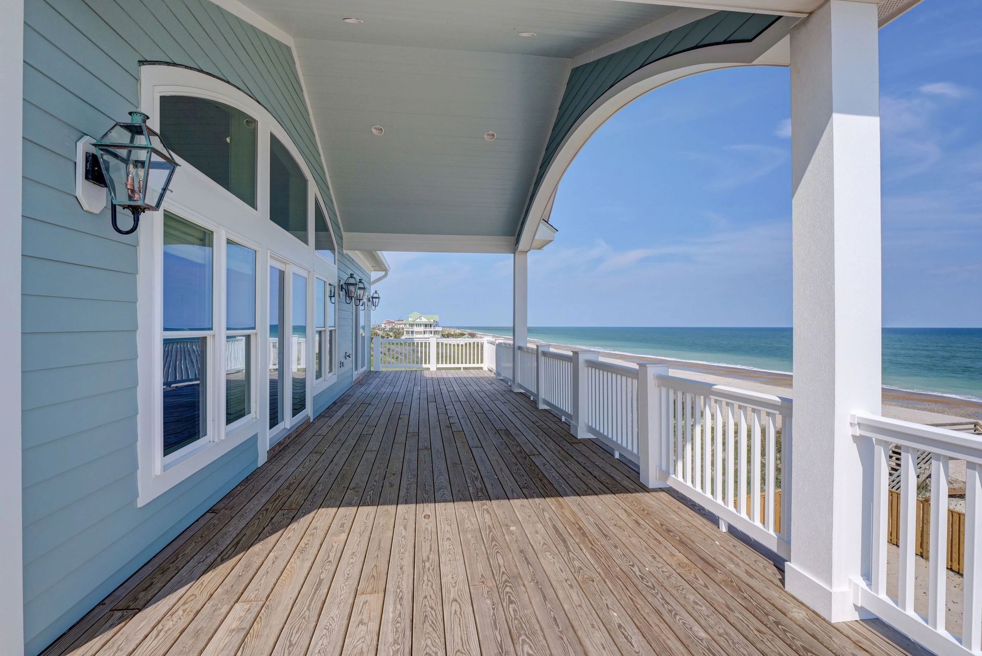 Beach house with light blue siding and a wooden deck overlooking the ocean.