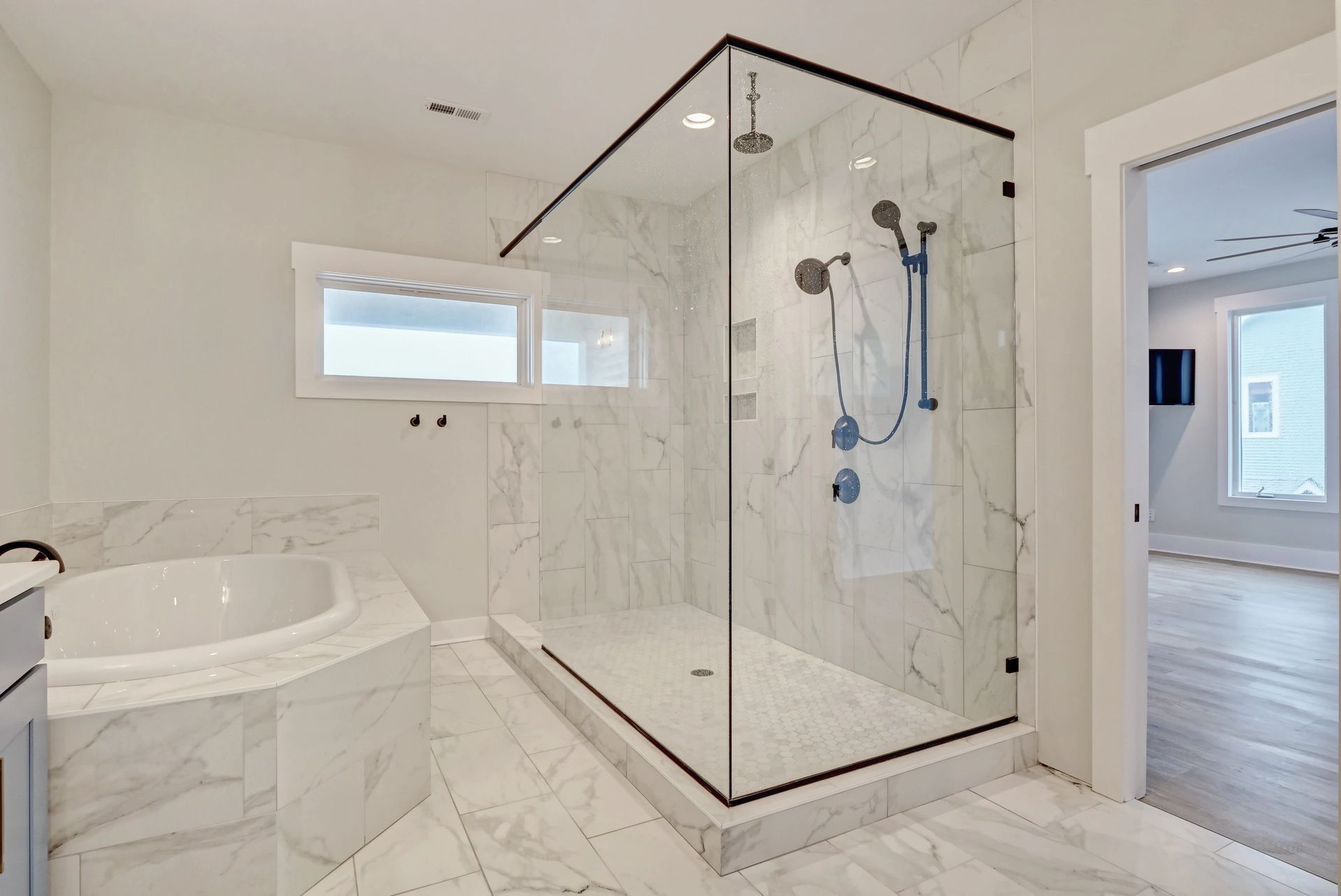 Bathroom with marble tile, large glass shower, and white soaking tub.