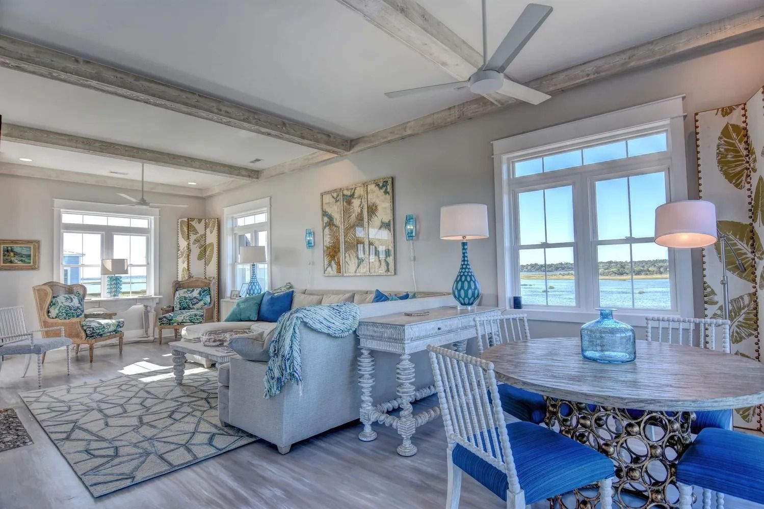 Coastal living room with light blue and white decor, water view through windows.