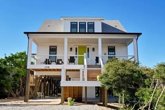 White beach house on stilts with a green door, porch, and clear blue sky.