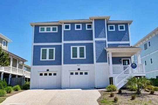 Blue and white multi-story beach house with garage doors, under a blue sky.