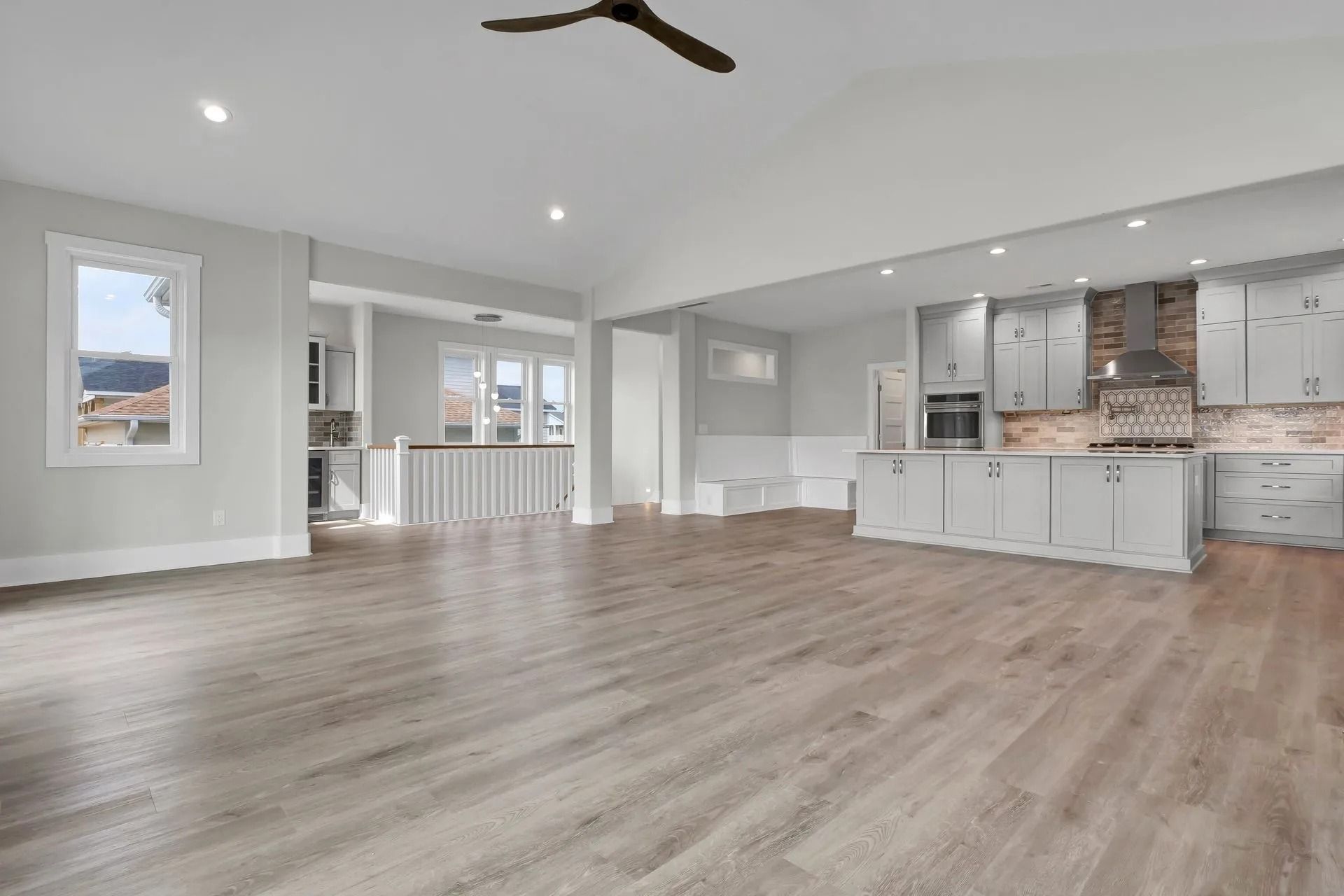 Open-plan kitchen and living area with gray cabinets, light wood floor, and recessed lighting.