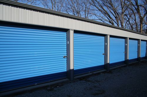 Row of blue storage unit doors along a building exterior in daylight