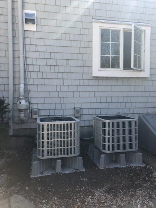 Two air conditioners are sitting outside of a brick building next to a window.