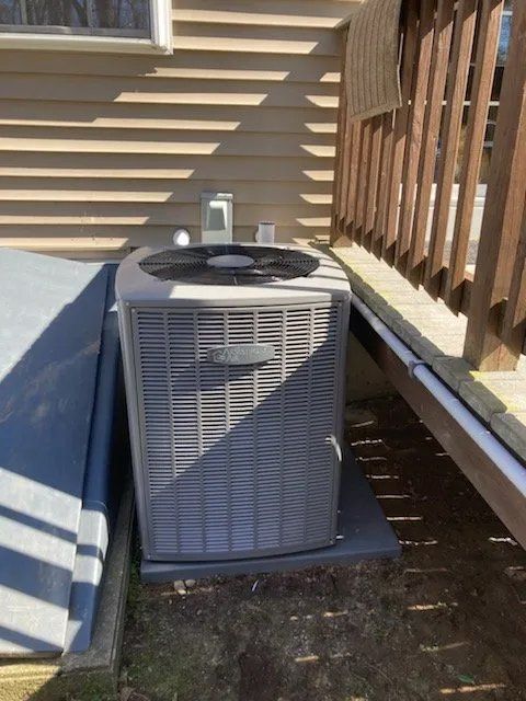 An air conditioner is sitting outside of a house next to a deck.