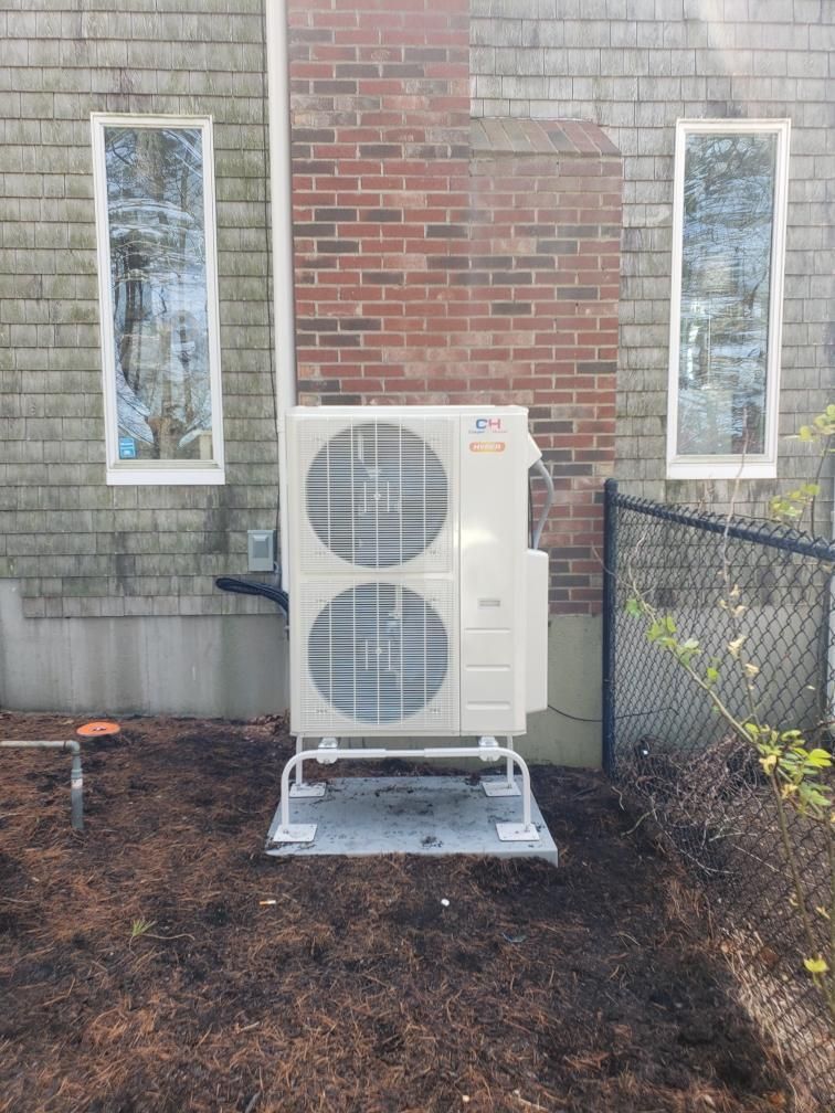 A large air conditioner is sitting in front of a brick building.