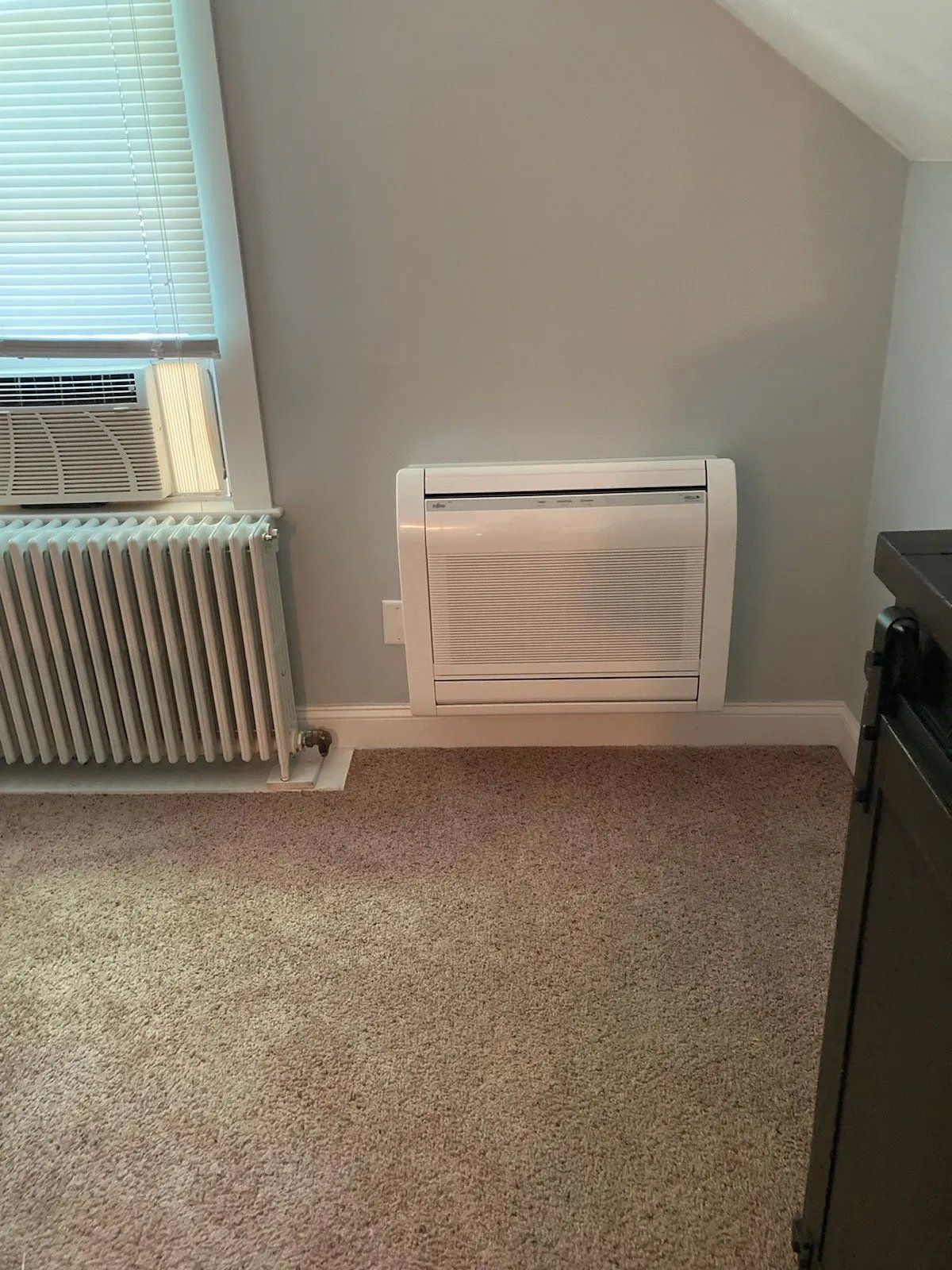 A room with a window , radiator , and air conditioner.