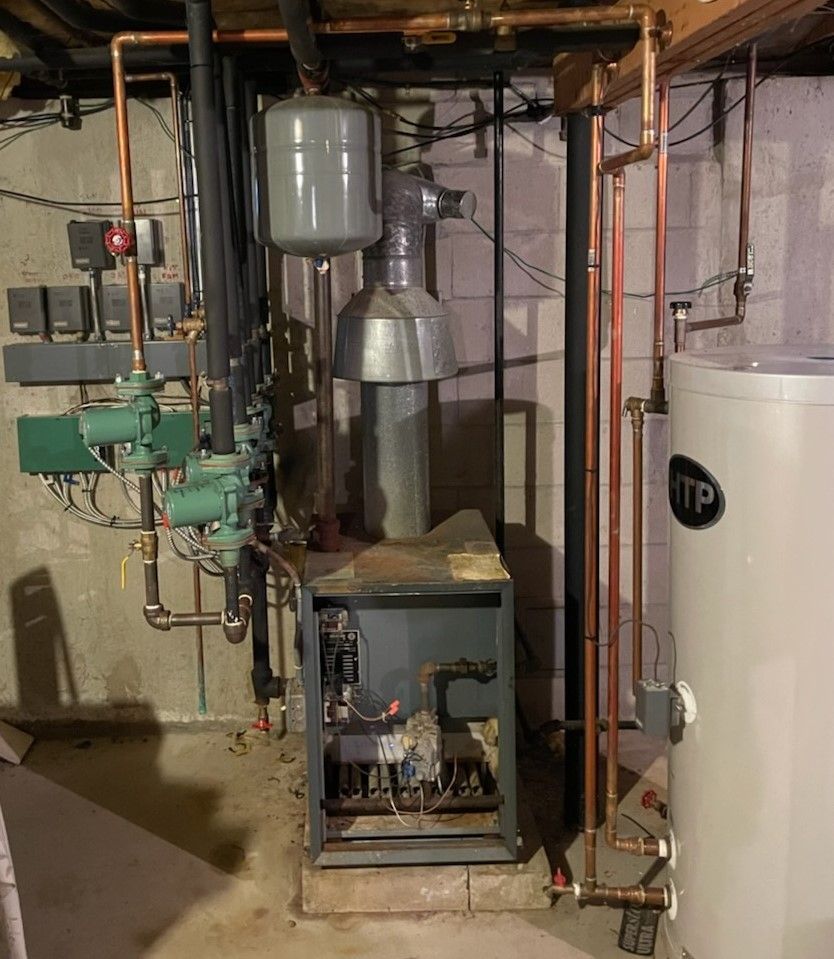 A boiler is sitting in a basement next to a water heater.