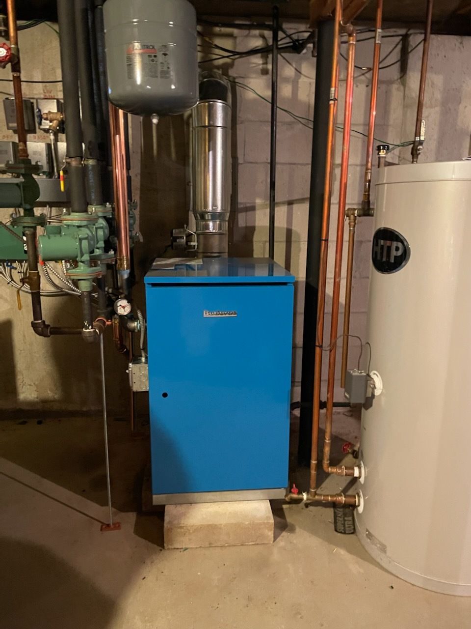 A blue boiler is sitting in a basement next to a white water heater.