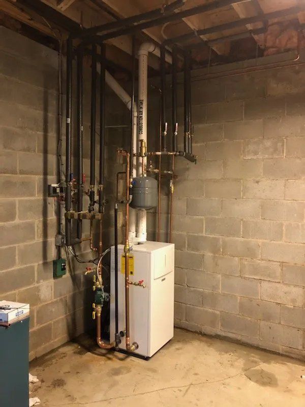A boiler is sitting in a basement next to a brick wall.