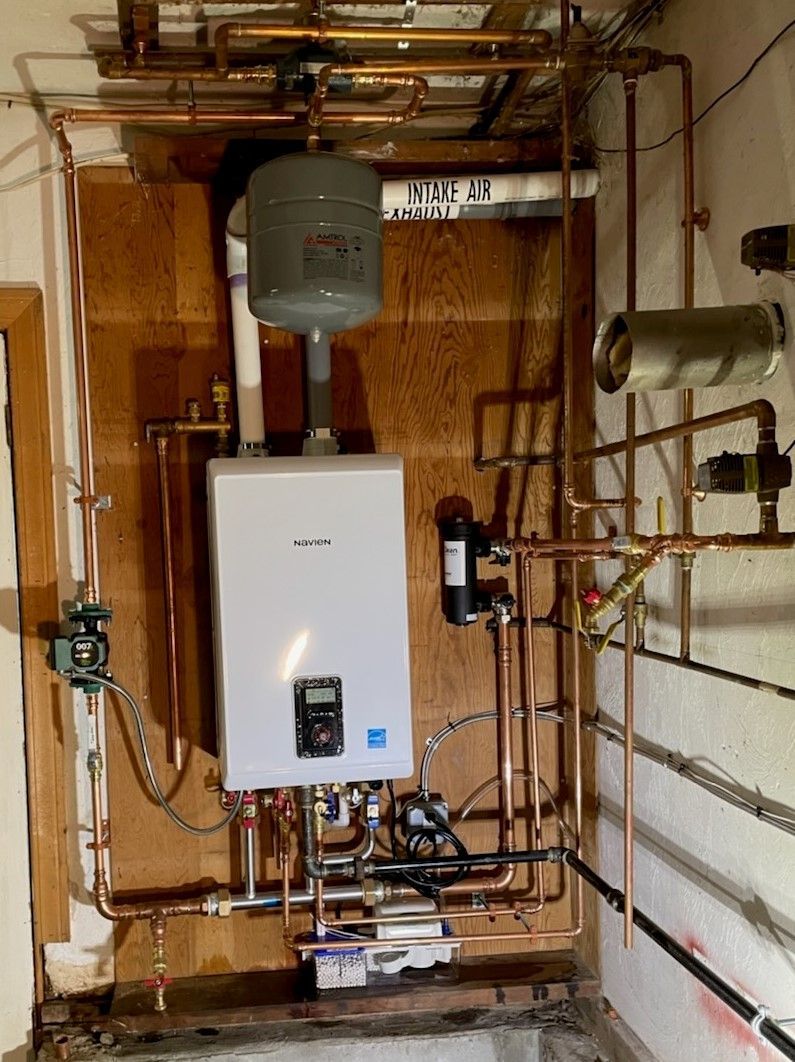 A room with a boiler and copper pipes on the wall.