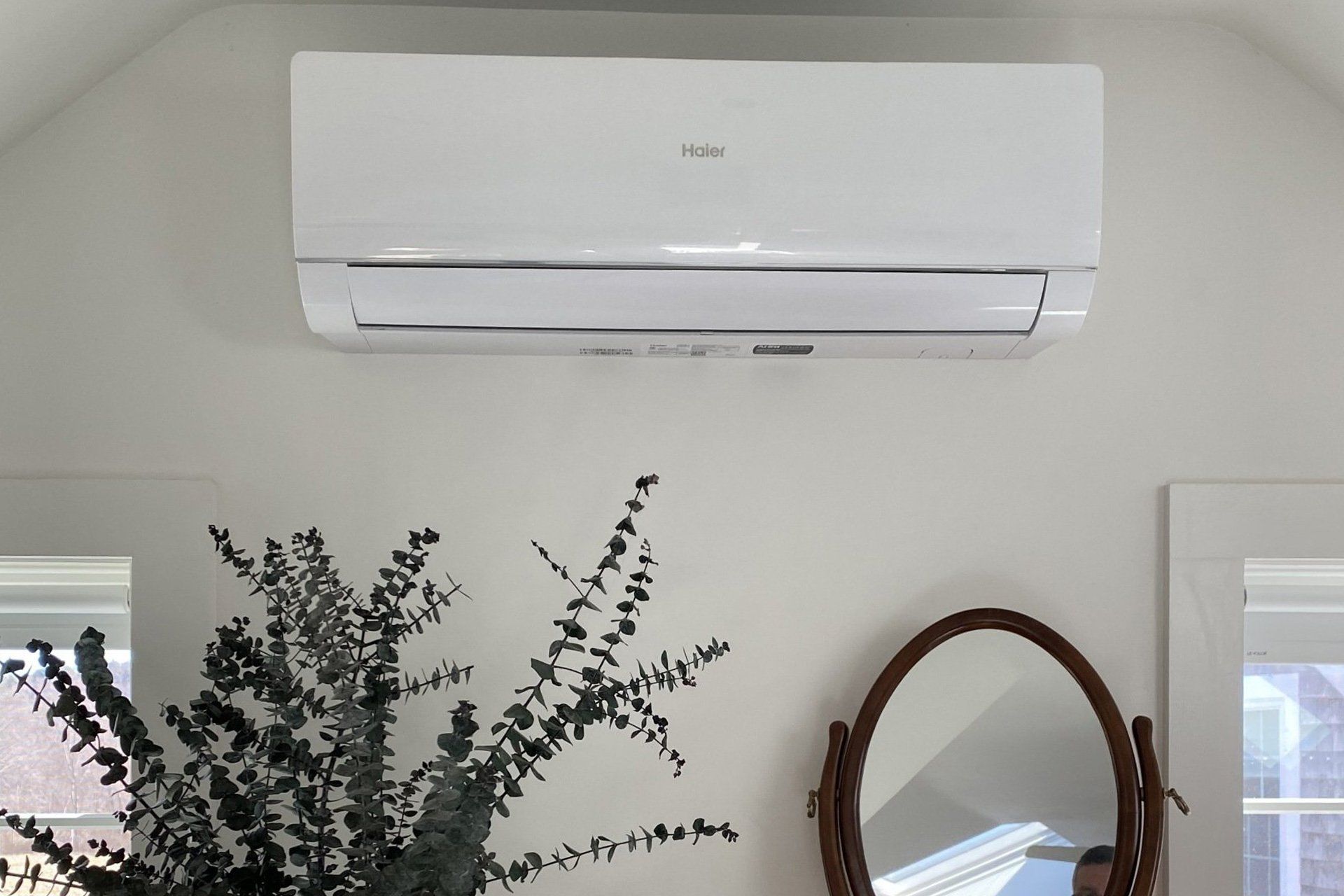 A white air conditioner is hanging on a white wall next to a mirror.