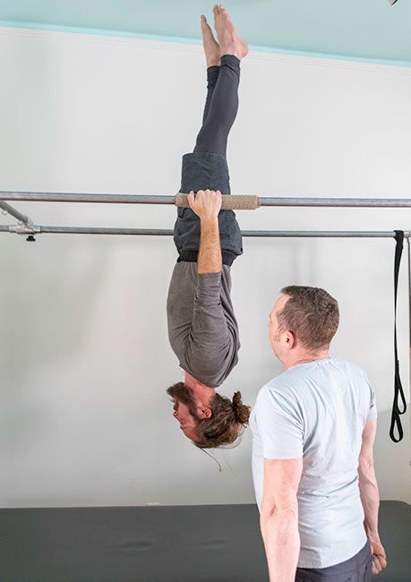 A man is helping a woman do a handstand on a bar.