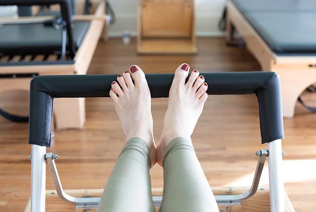 A woman is sitting on a pilates machine with her feet crossed.