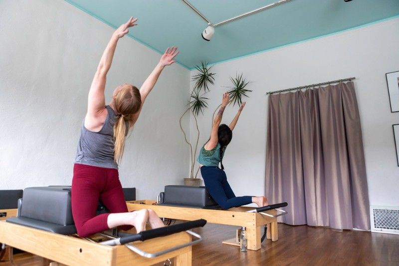 Two women are doing yoga on pilates tables in a gym.