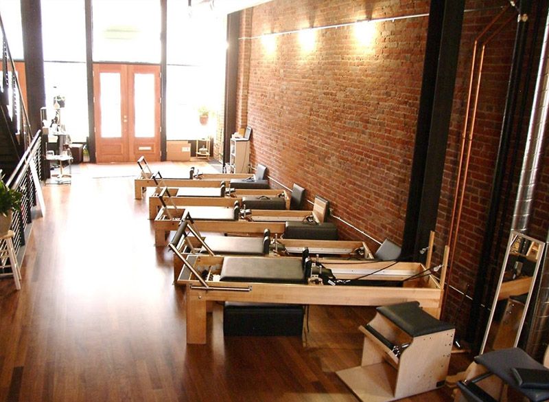A row of pilates machines in a room with a brick wall