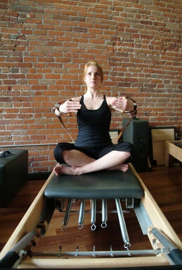 A woman is sitting on a pilates machine in front of a brick wall.