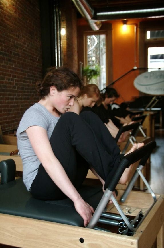 A woman sits on a pilates machine with her legs crossed