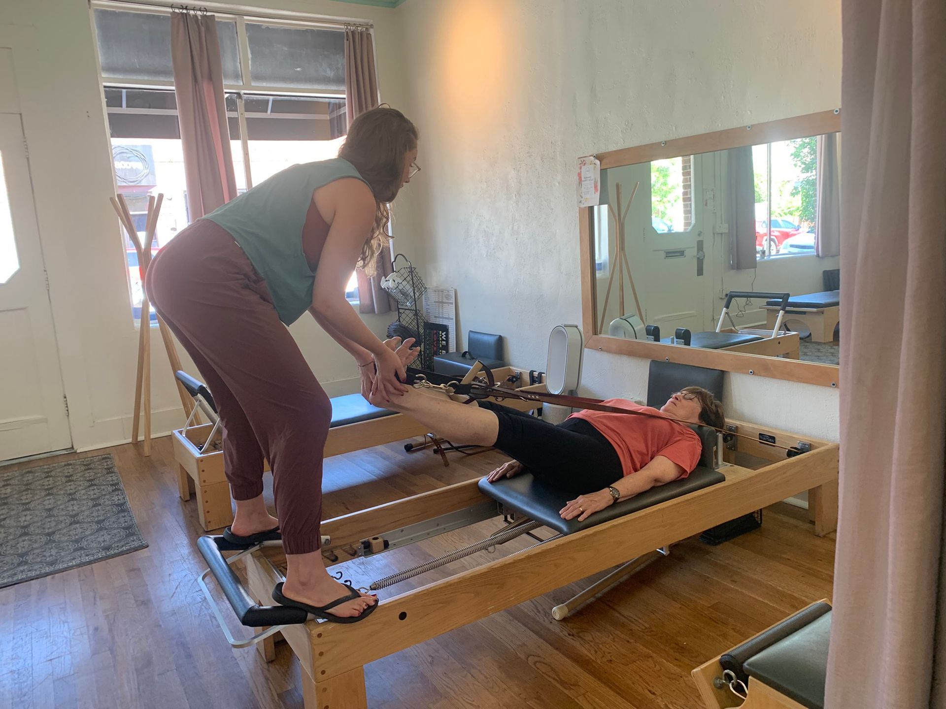 A woman is standing next to a woman laying on a pilates machine.