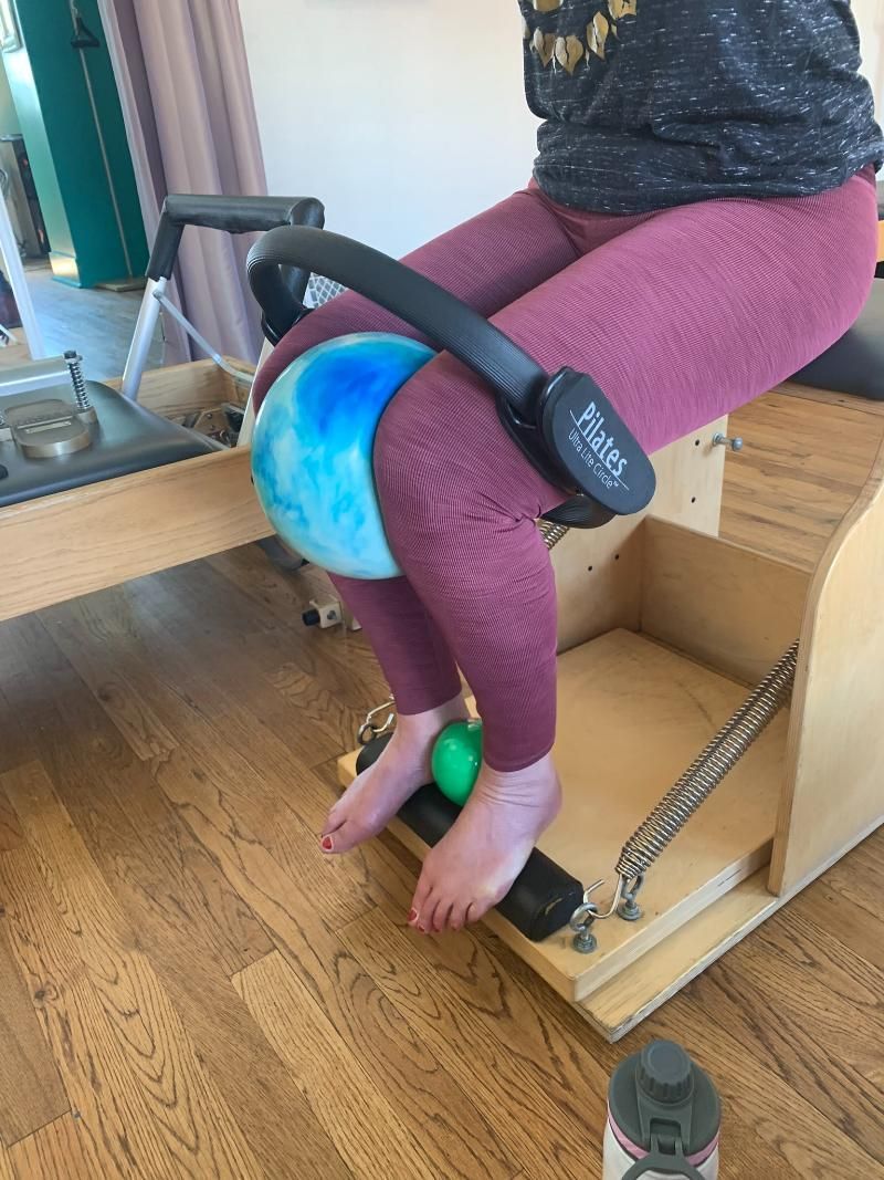 A person is sitting on a pilates machine with a ball on their knee.