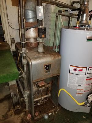 A water heater is sitting next to a boiler in a basement.