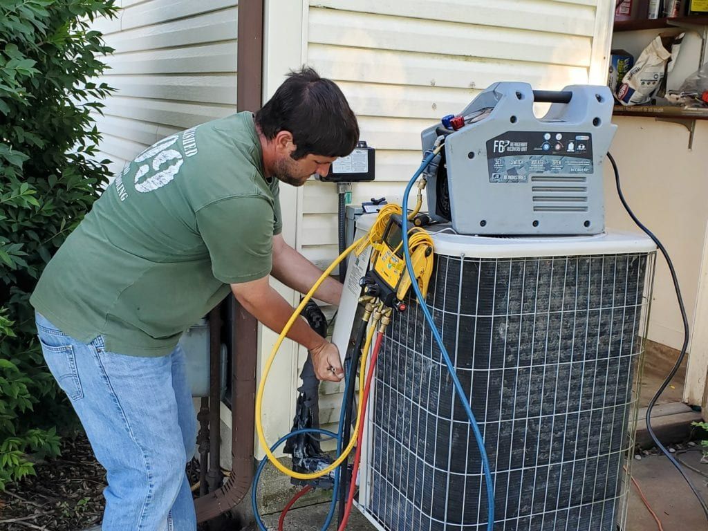 A man is working on an air conditioner outside of a house.