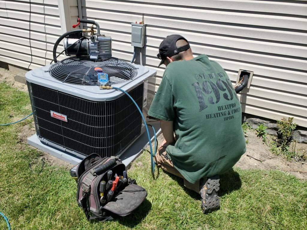 A man in a green shirt is working on an air conditioner.