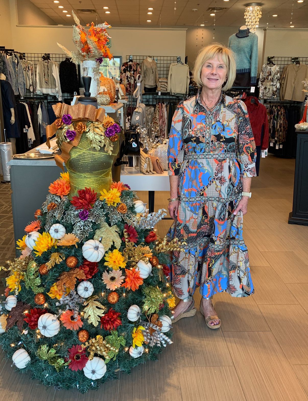 Woman in a colorful dress poses by a fall-themed mannequin in a retail store.