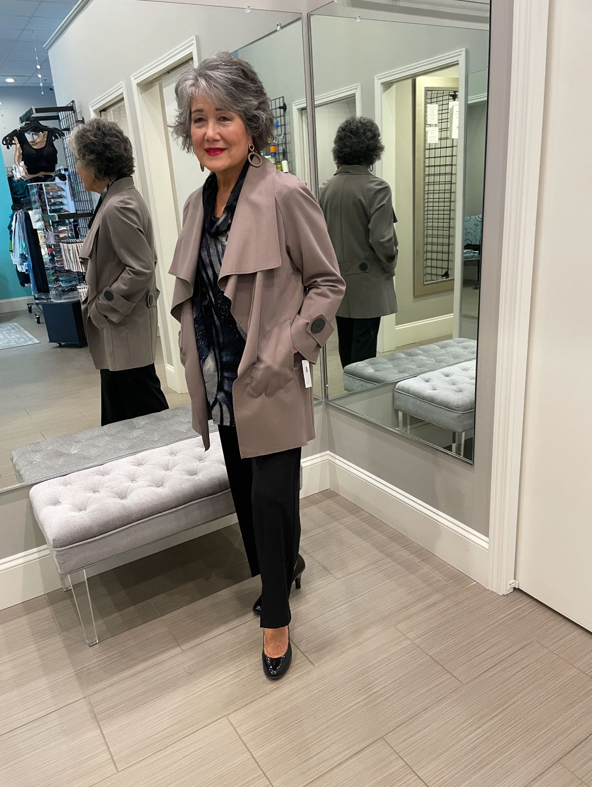 Woman in a coat and black pants in a store, standing near a mirror.