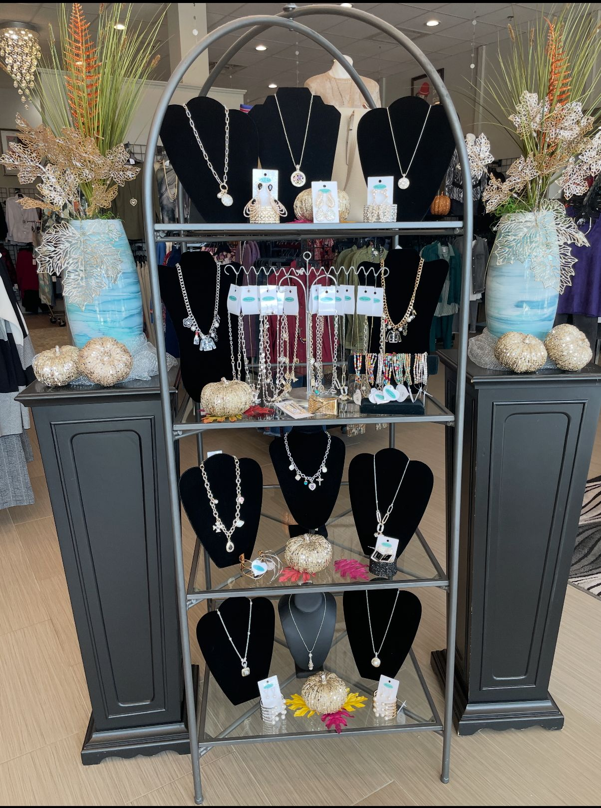 Jewelry display with necklaces on black velvet stands, silver shelving, and decorative flowers.