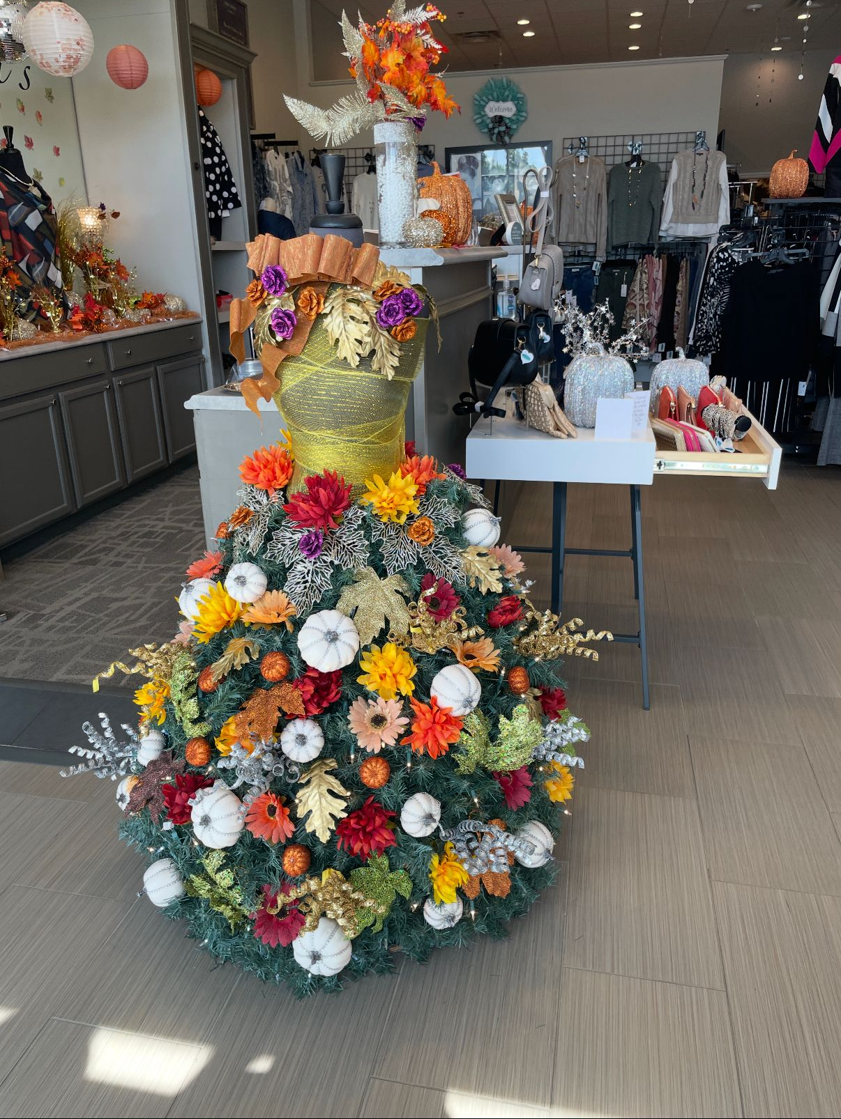 Fall-themed dress-shaped display with pumpkins, flowers, and foliage in a retail store.