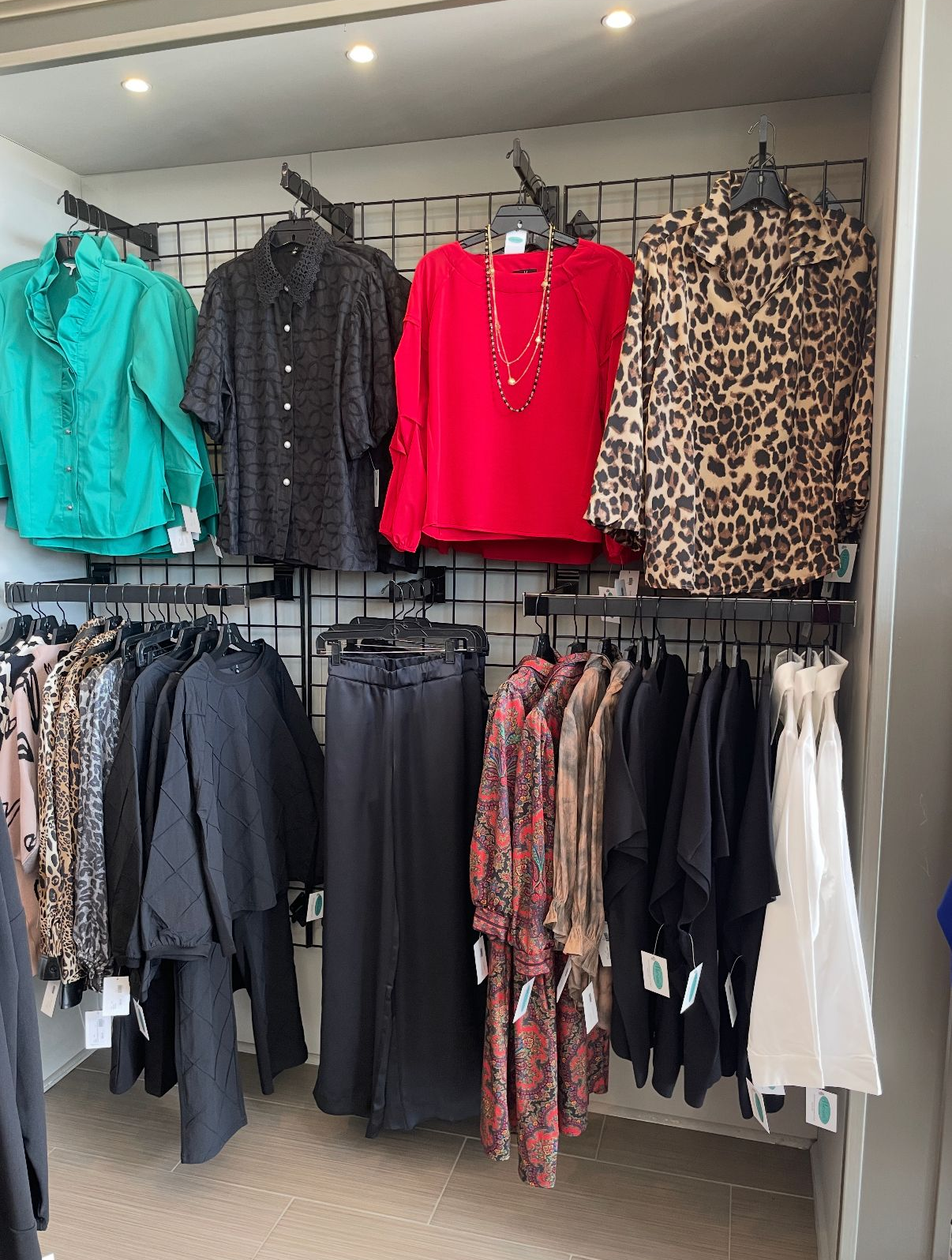 Clothing store display with shirts in green, black, red, and leopard print above clothing racks.