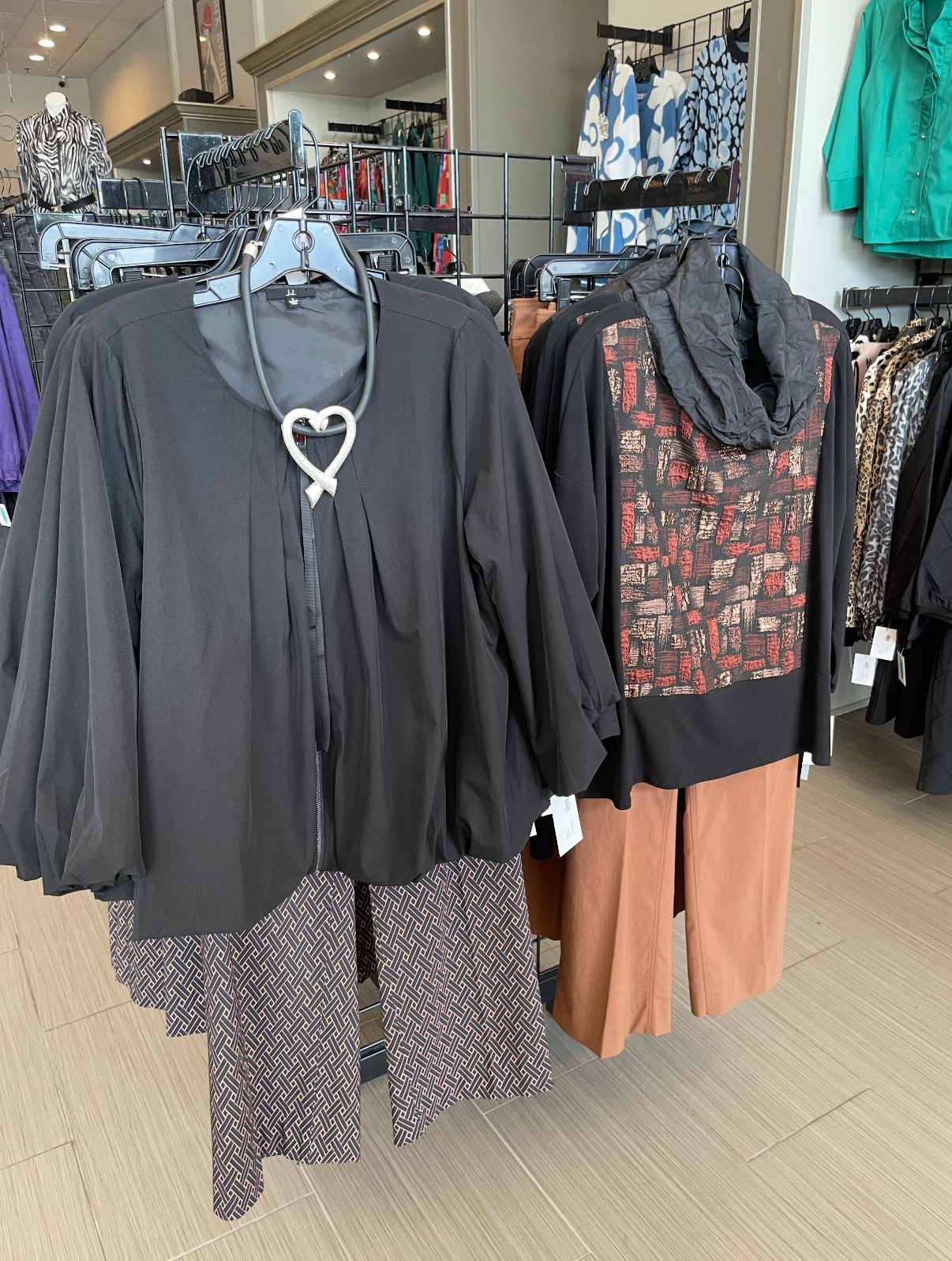 Clothing store display: black jacket with patterned pants; sweater with brown pants.