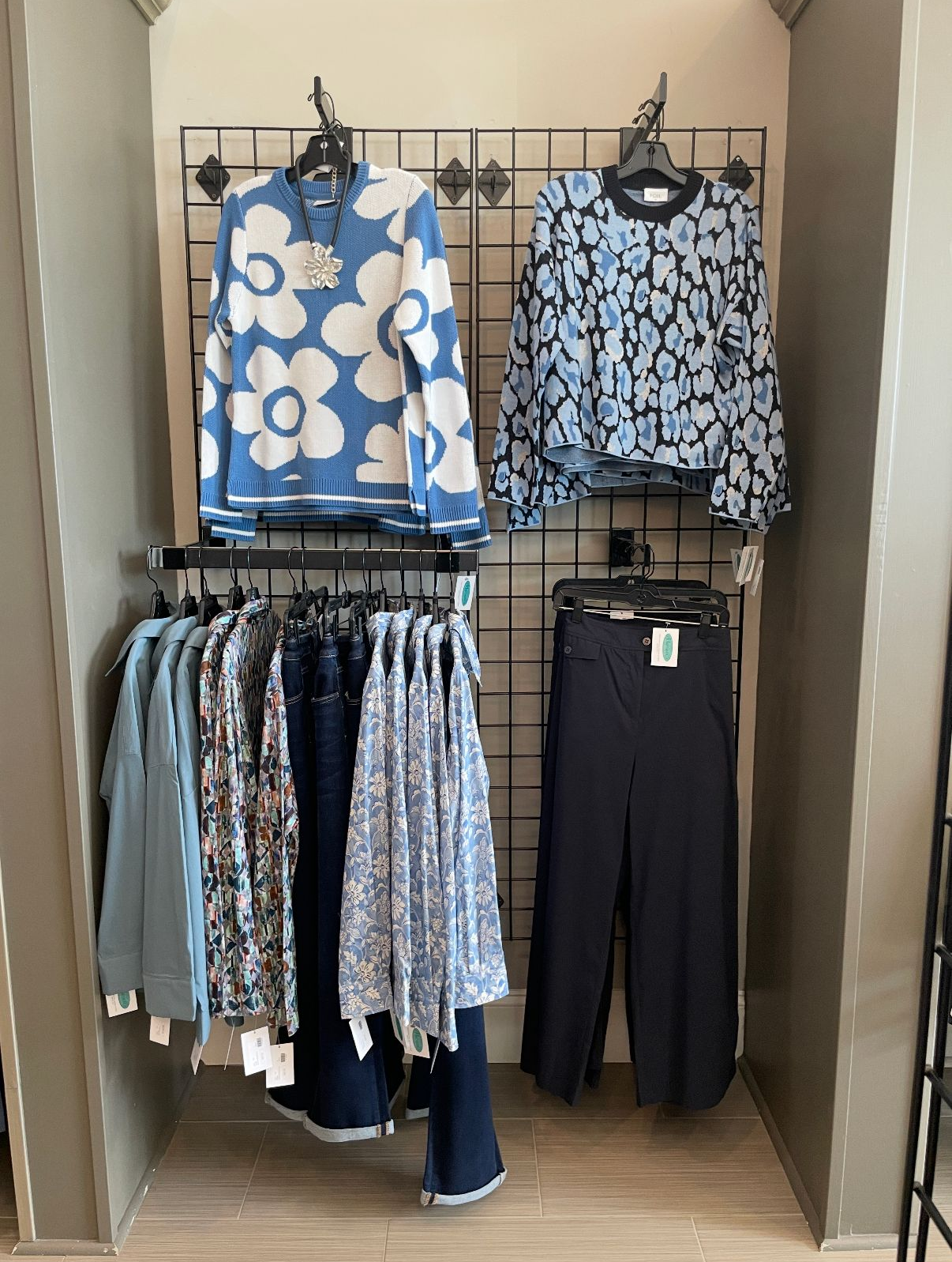 Clothing display: blue floral sweaters and various blue pants hanging on racks, in a store.