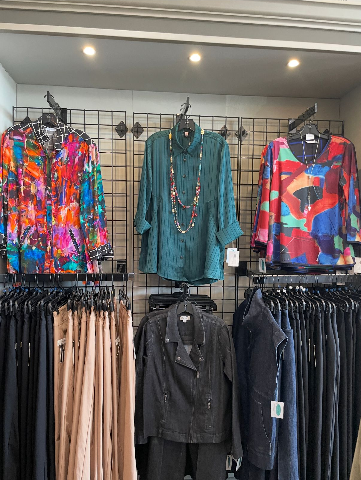 Clothing store display with colorful tops on the wall, black pants below.
