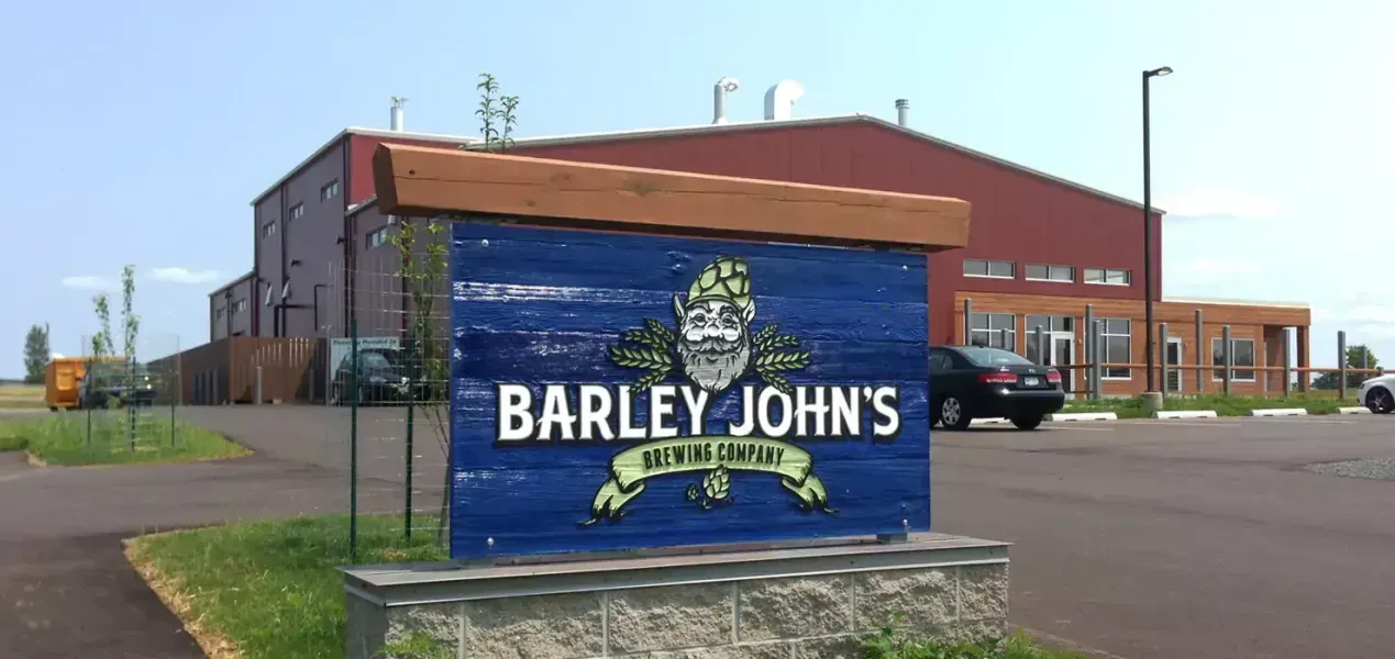 Sign for Barley John's Beer in front of a red building with a parking lot.