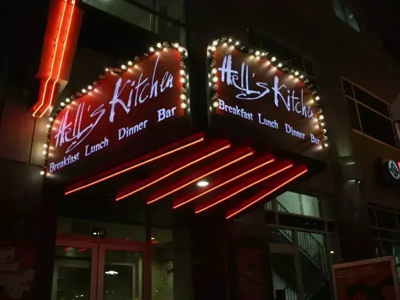 Hell's Kitchen restaurant at night with illuminated sign, red neon accents, and string lights.