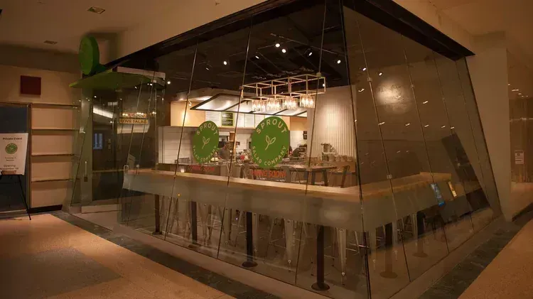 A restaurant storefront with glass walls, interior seating, and a green logo.