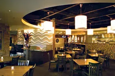 Restaurant interior with tables, chairs, pendant lights, and decorative wavy wall.