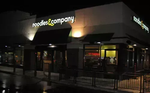 Noodles & Company restaurant exterior at night with illuminated sign and awnings.
