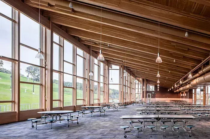 Spacious dining hall with large windows overlooking green fields. Wooden beams and tables line the room.