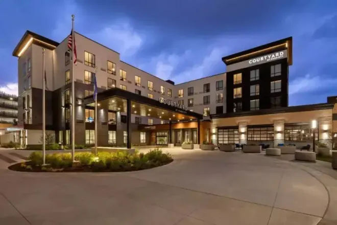 Courtyard hotel exterior at dusk with lights on, front entrance, and US flag.