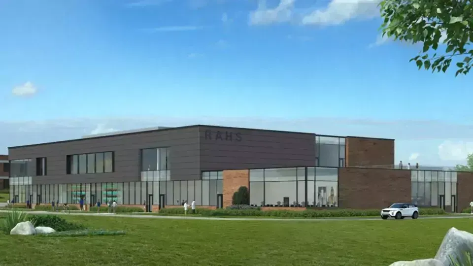 Modern building with dark exterior and large windows, on a green lawn, under blue sky.