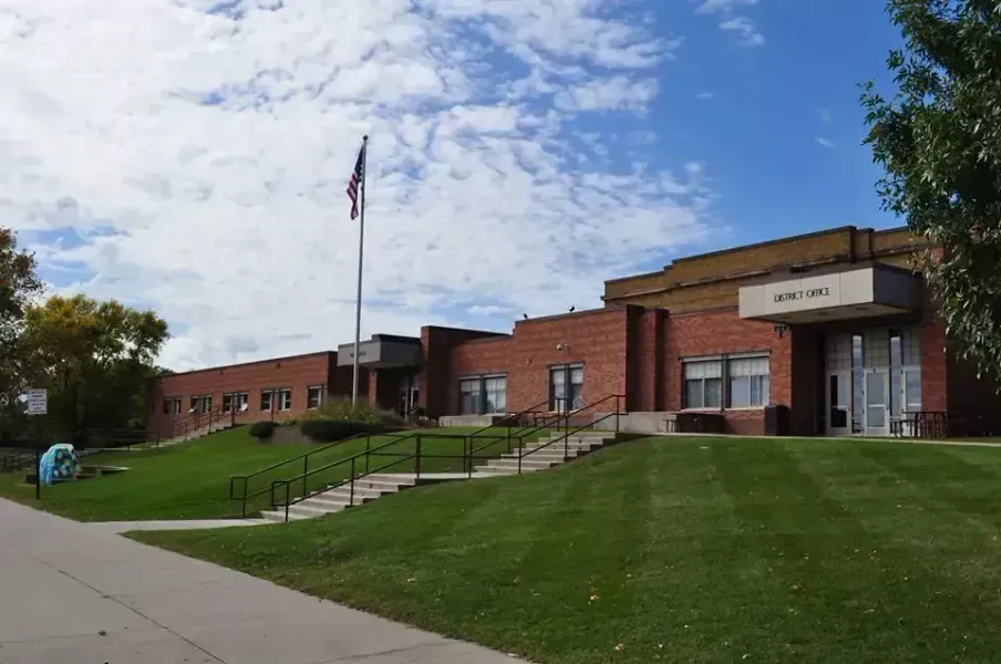 Brick building with grass lawn, American flag. Sign above door reads