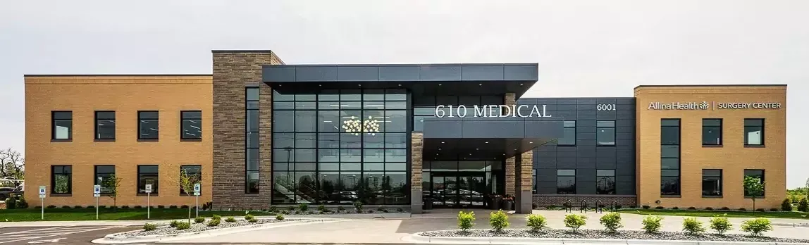 Exterior of a modern medical building with glass entrance, stone accents, and muted tan and gray colors.